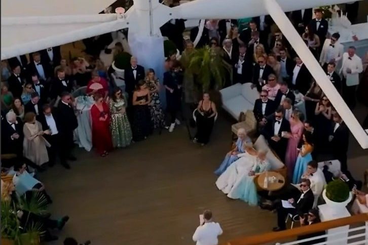 A black-tie crowd seen from above, standing in a ring around an empty floor