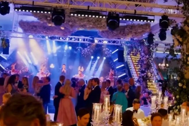 A gala hall under the venue lighting rig, guests standing between the tables and the stage